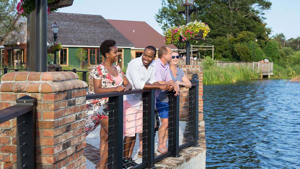 Two couples leaning against a brick and front railing looking out over the water with a green building behind them at Barefoot Landing in Myrtle Beach, South Carolina, USA